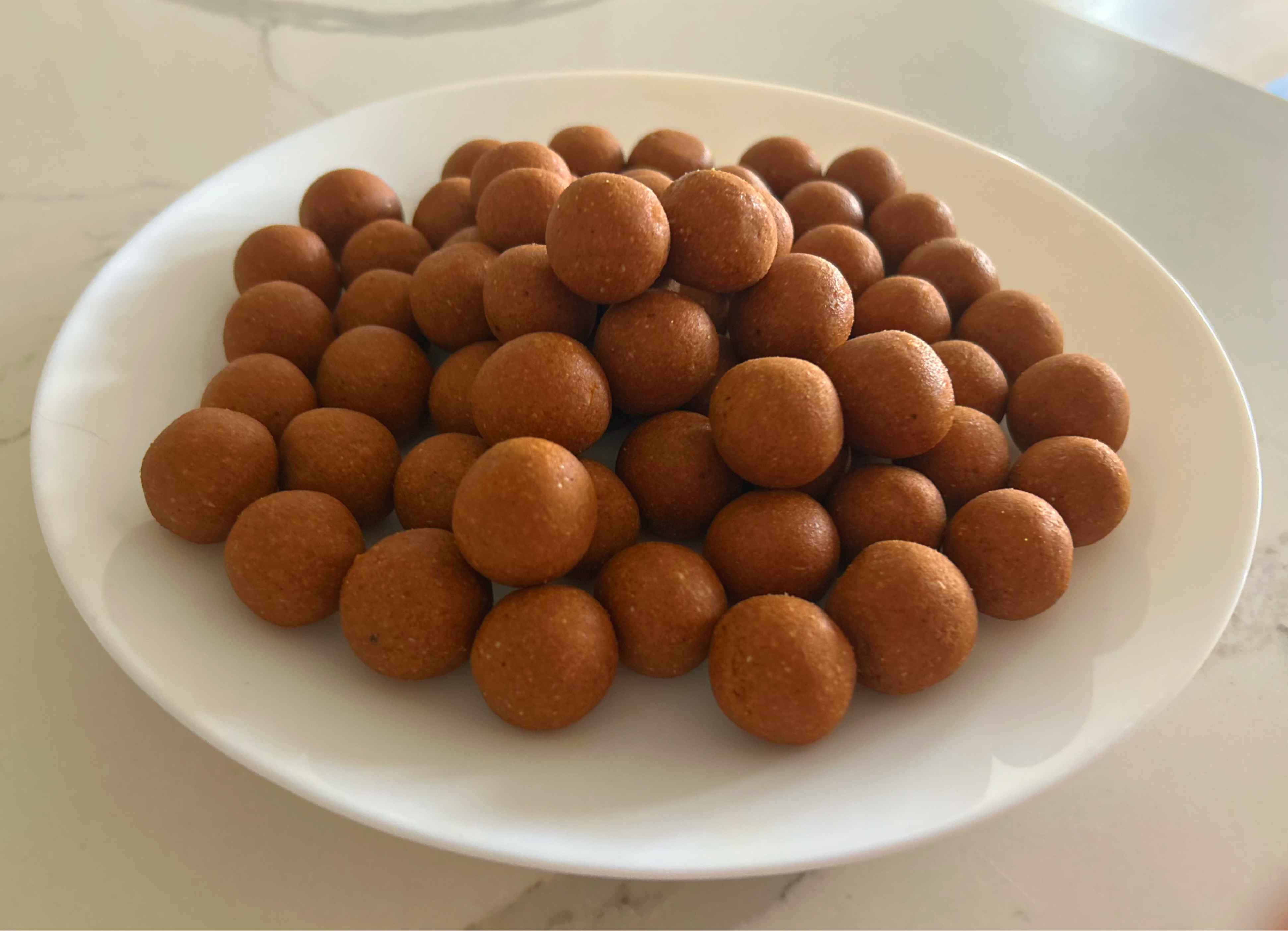 A white plate piled with golden-brown, hand-rolled laddoos